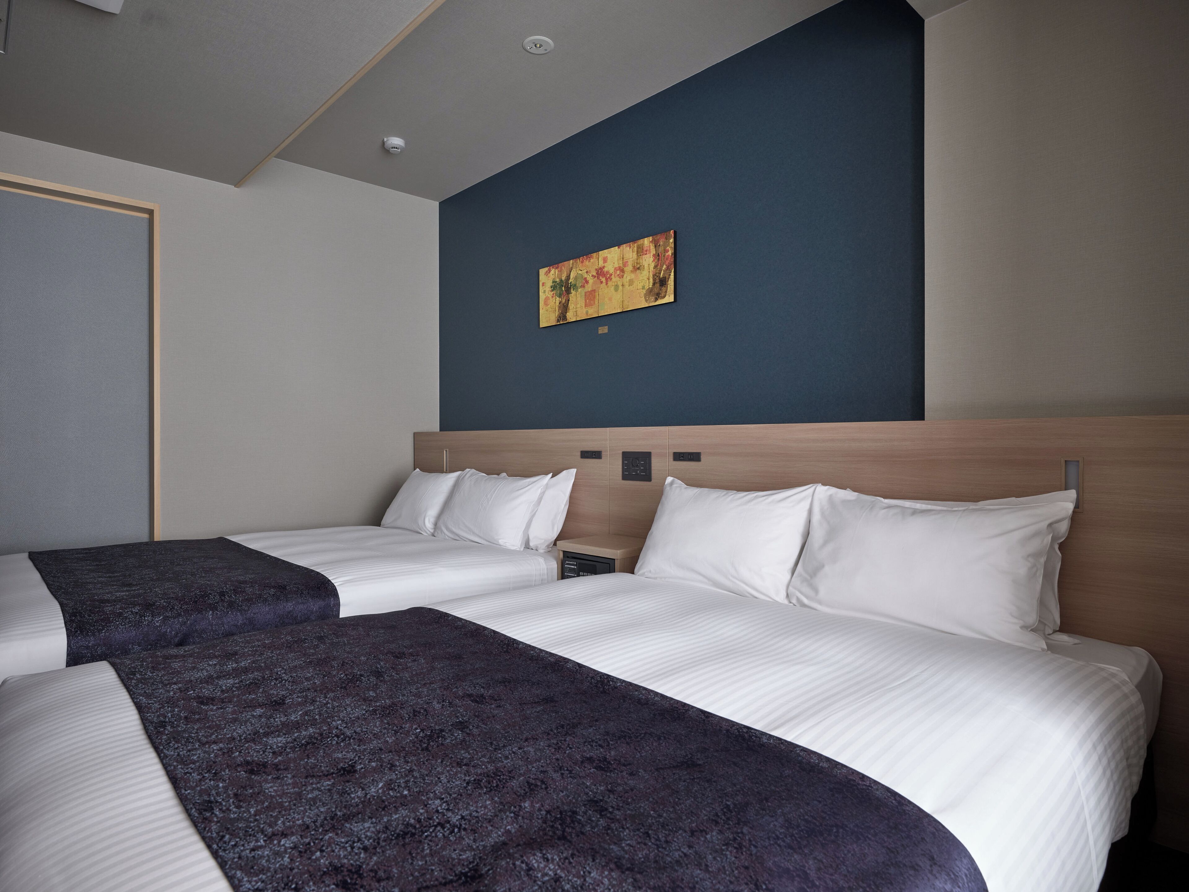 Une chambre d’hôtel avec deux lits, un mur d’accent de couleur bleu foncé et un tableau.