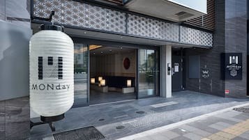 A modern hotel entrance with a reception desk, a waiting area, and a sign indicating "MONDAY" and "Hotel MONDAY."