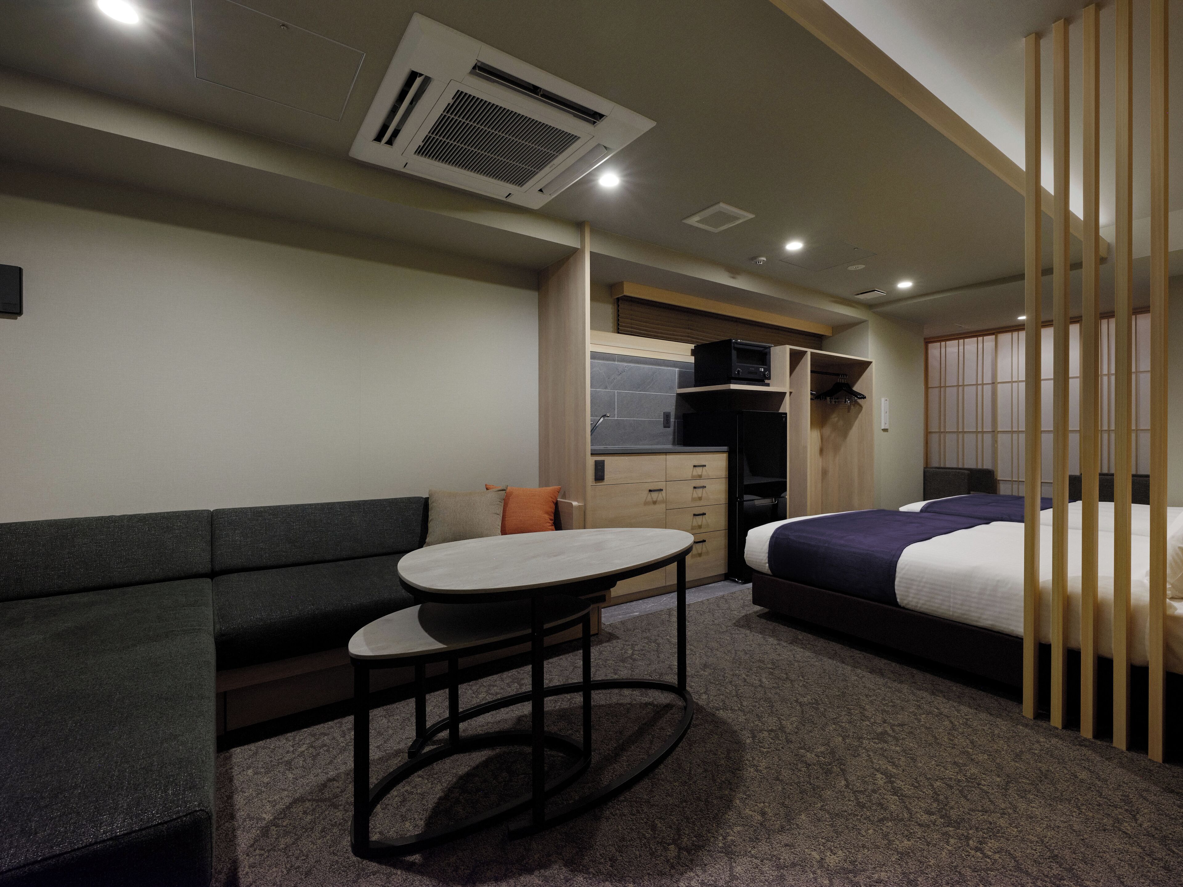 Une chambre d’hôtel compacte comprenant un canapé, une petite table, un lit, une kitchenette et une porte coulissante.