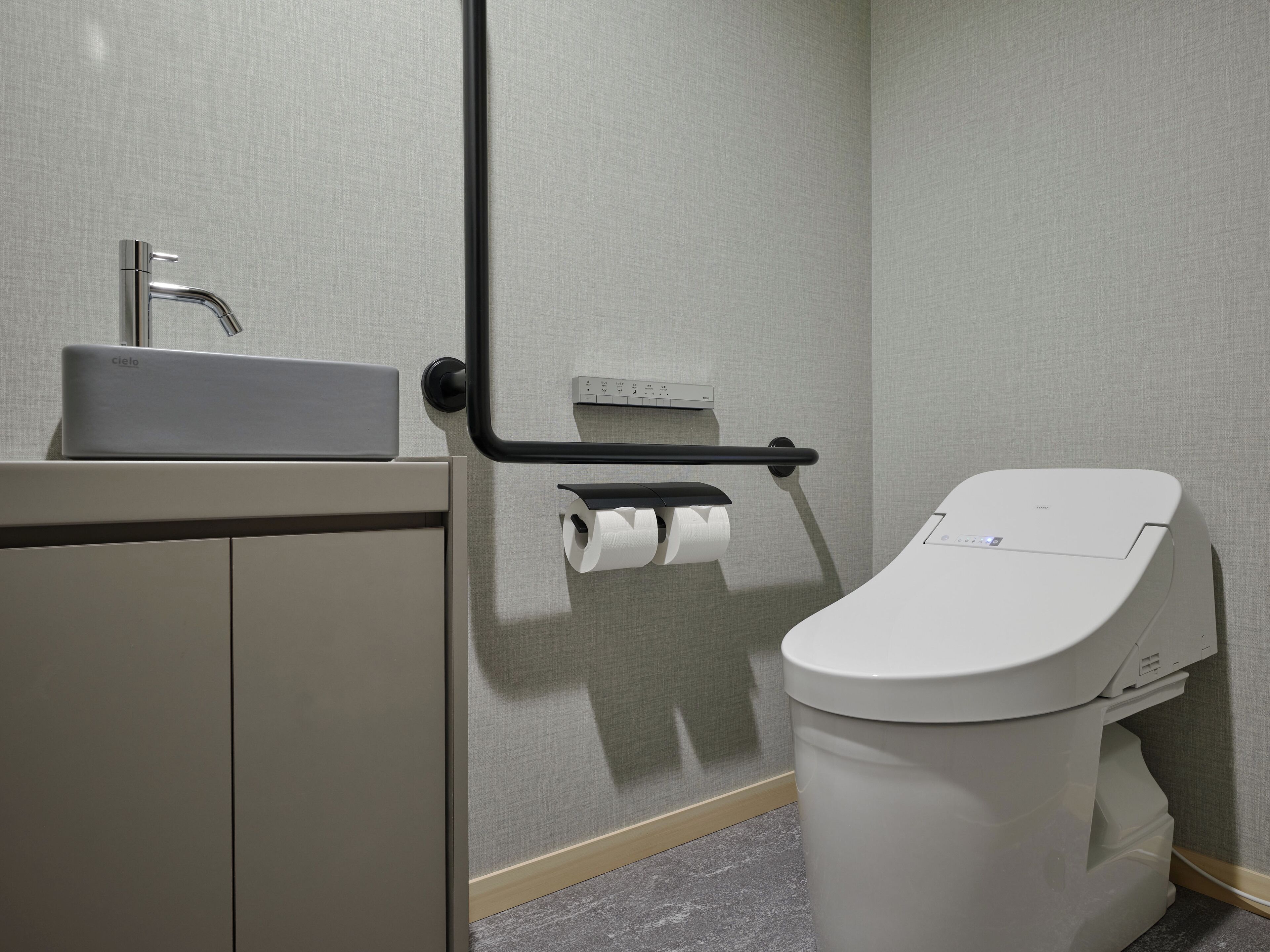 A modern bathroom with a toilet, a sink, and a paper towel dispenser.