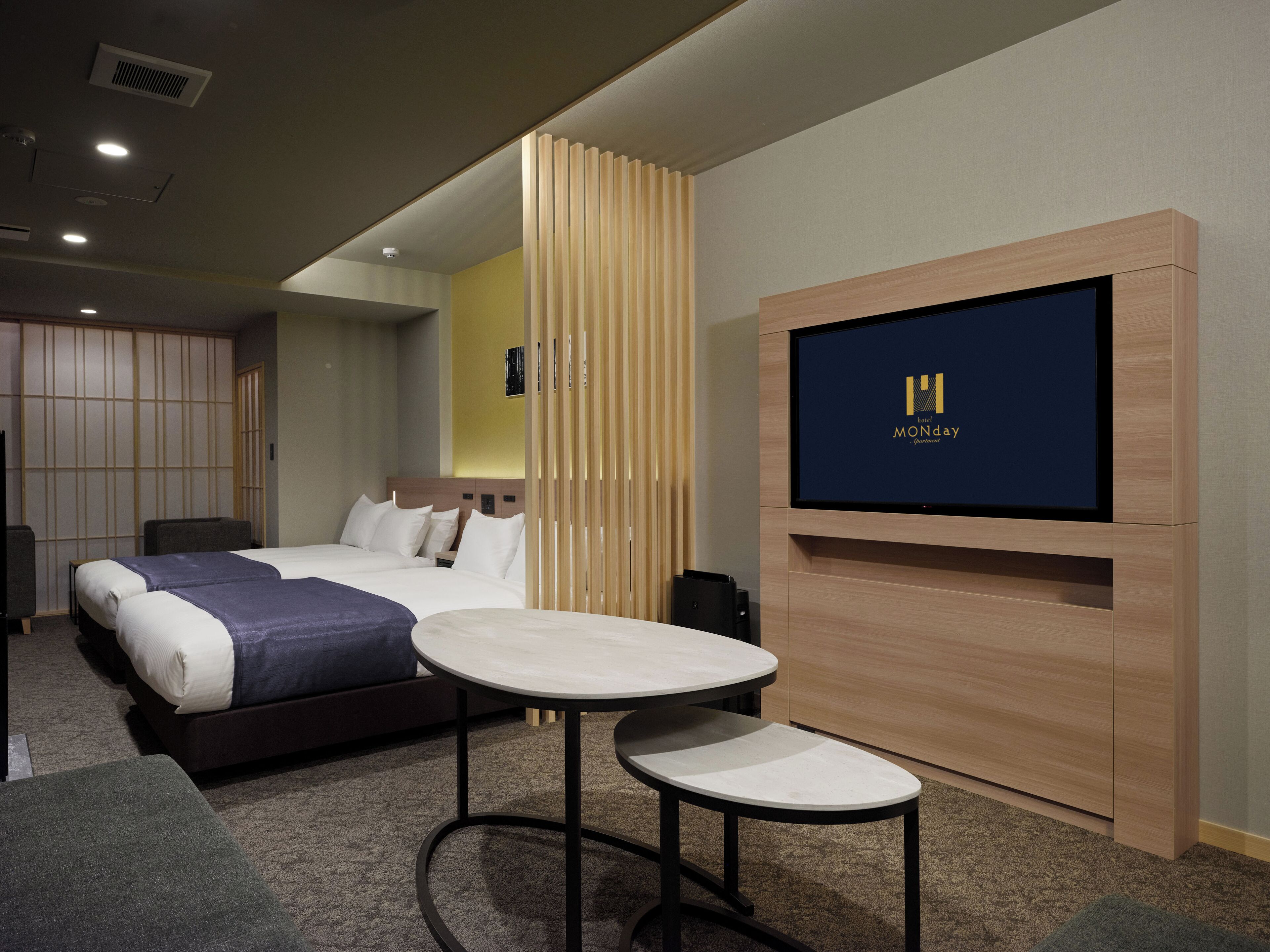 A hotel room with two beds, a TV on the wall, and a small table.