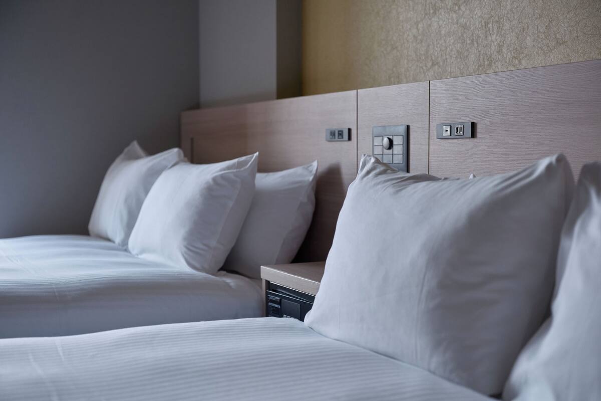 Habitación de hotel con dos camas, cada una con ropa blanca y almohadas. Se observan paneles de control en los cabeceros para los servicios de la habitación.