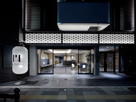 A modern building entrance with a geometric patterned facade, a reception area with a counter and seating, and a visible sign with the word "MONDAY".