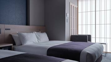 A hotel room with two beds, a wooden headboard, a nightstand, a desk, and a large window with vertical blinds.