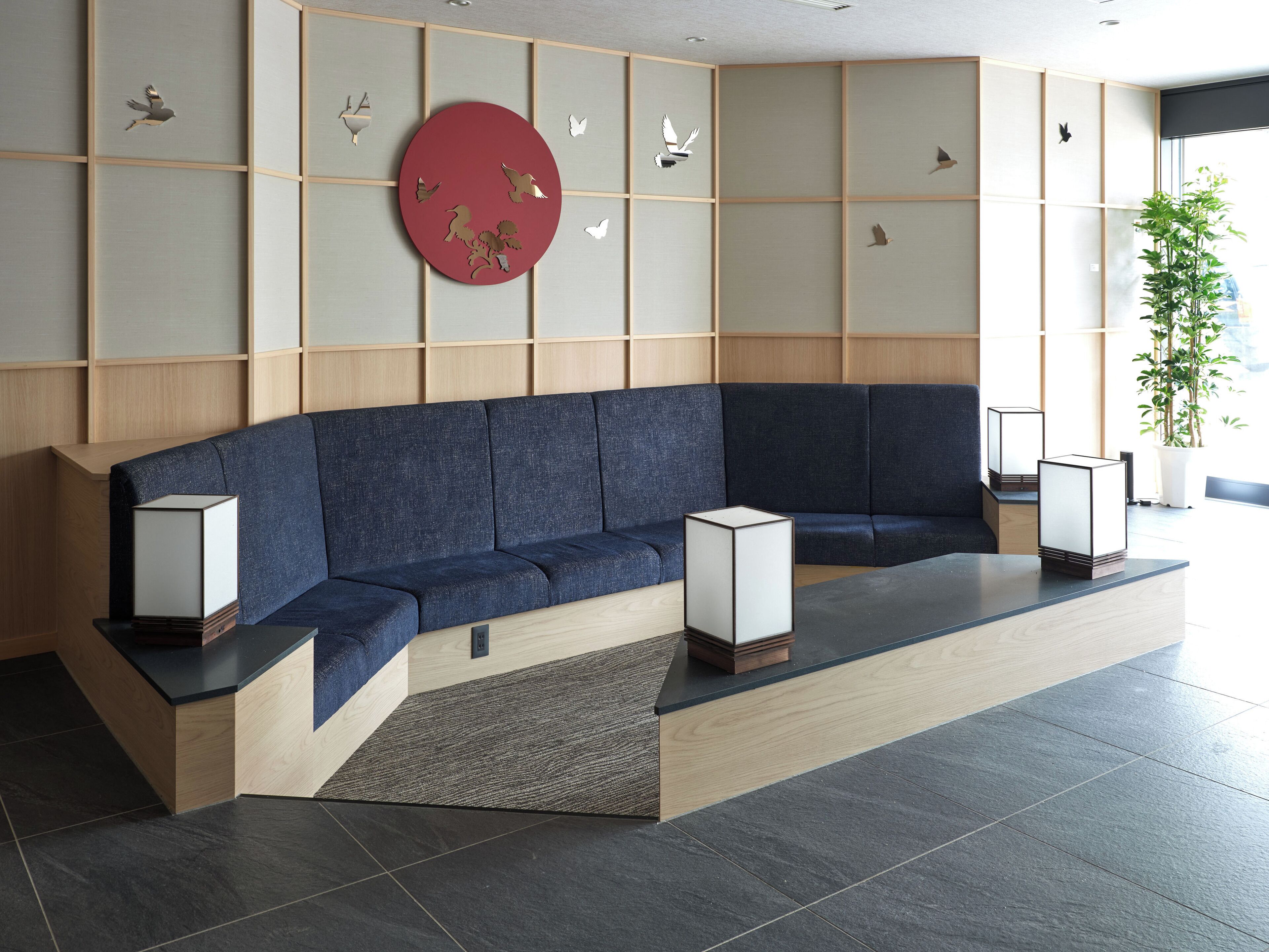 A modern waiting area with a blue sofa, two wall-mounted lamps, and a large red circular artwork.