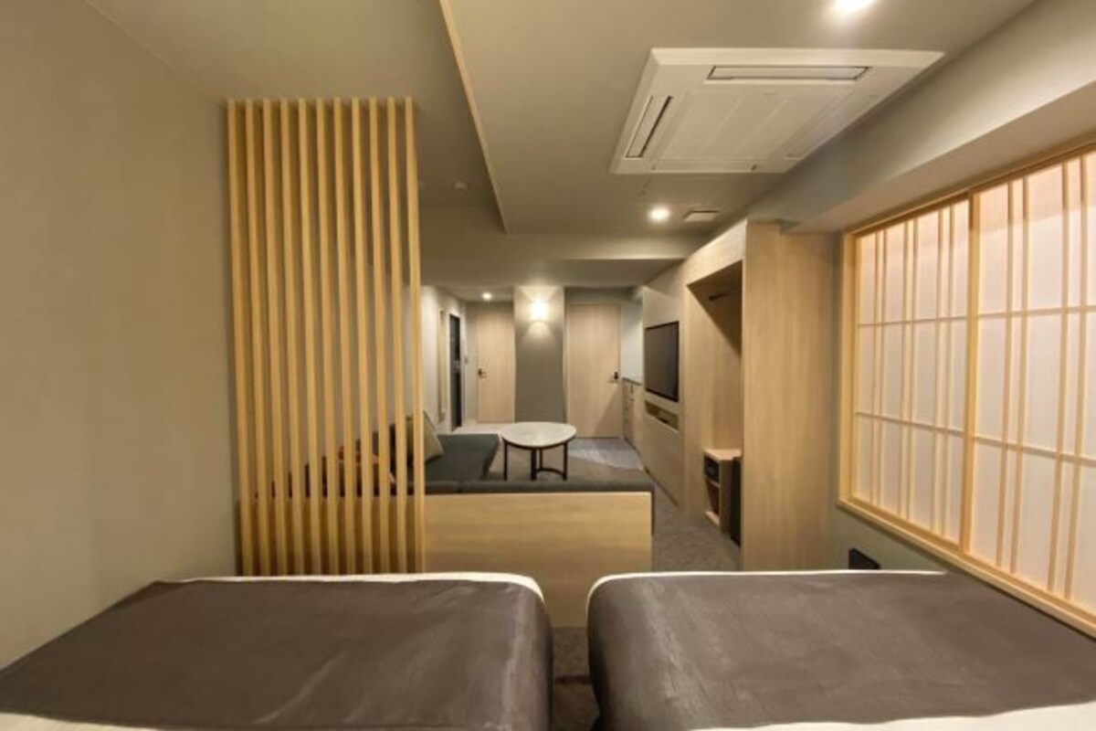 A hotel room with two beds, a small table, a TV, and a sliding door.