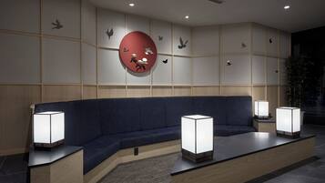 Un espace d’attente moderne avec un canapé bleu foncé, deux lampadaires et une grande décoration murale circulaire rouge.
