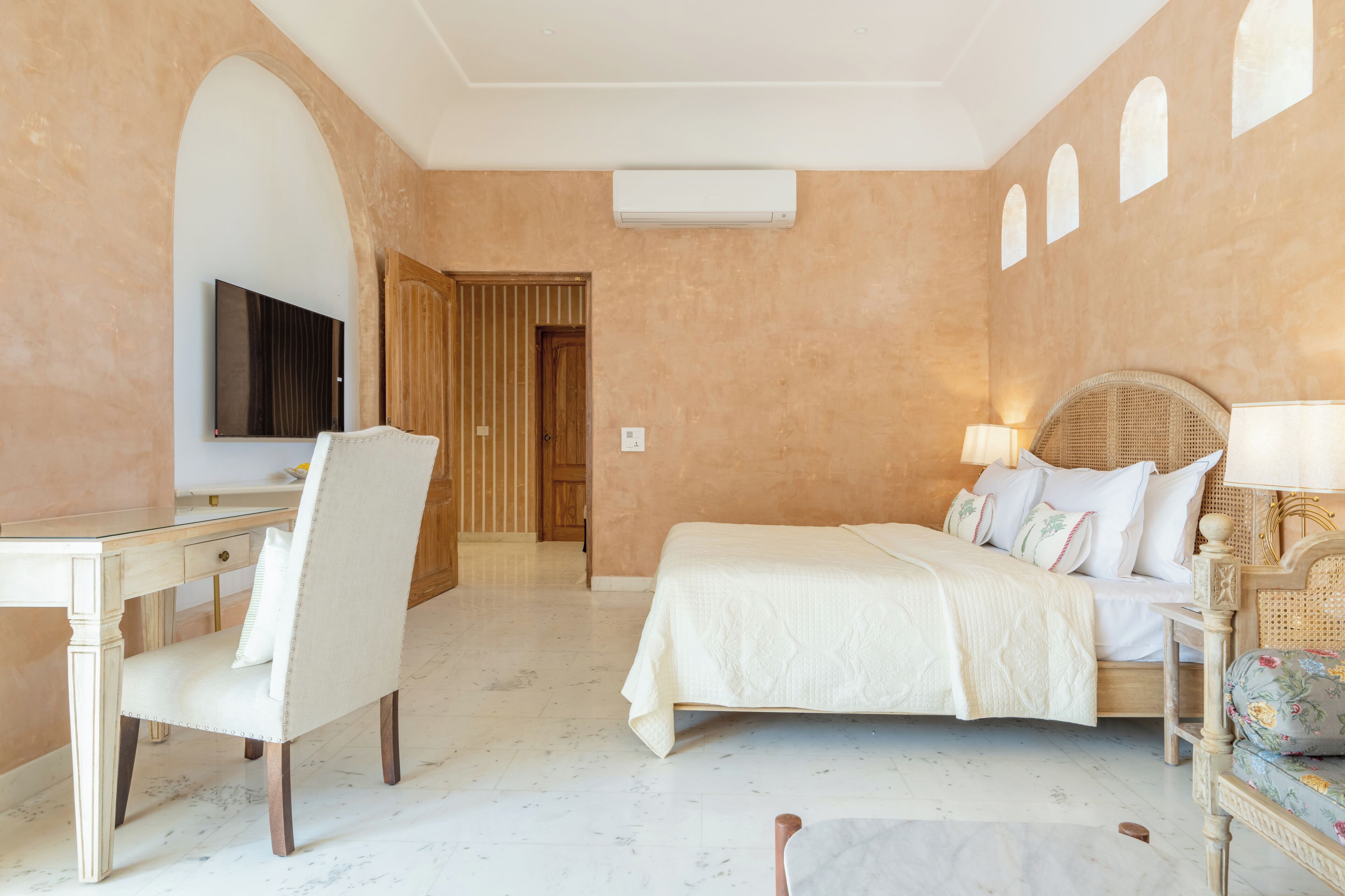 A hotel room with a bed, a desk, a chair, a television, and a door leading to another room.