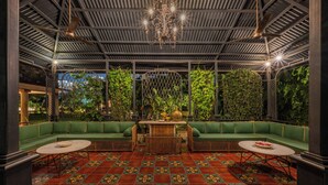 Un área de estar con asientos acolchados verdes, una mesa central, suelo estampado y techo con candelabro.