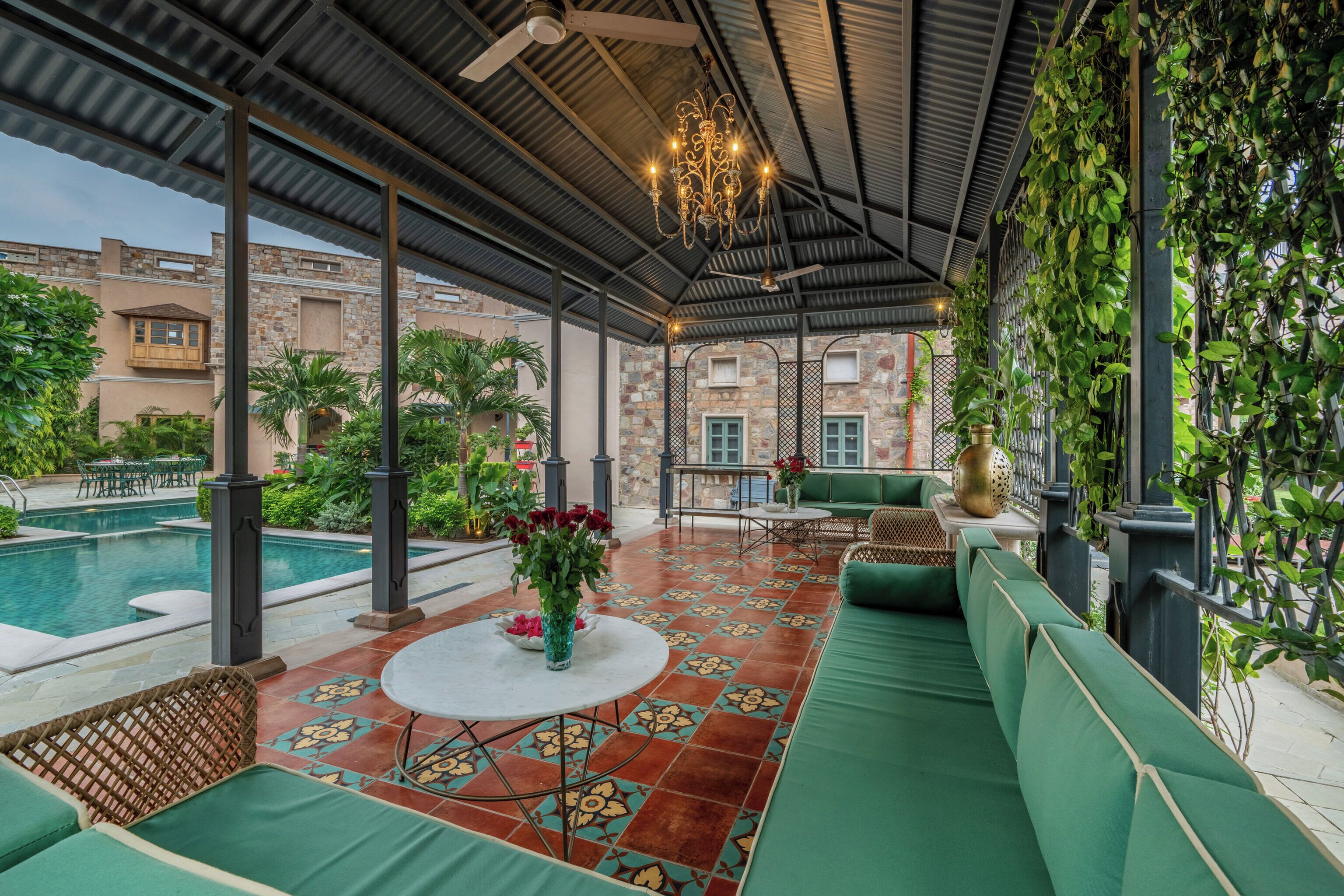 A covered outdoor seating area with a pool, green furniture, and decorative plants.