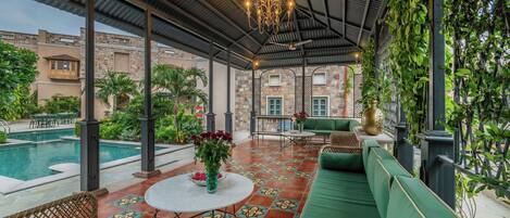 A covered outdoor seating area with a pool, green furniture, and decorative plants.