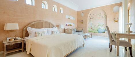 A spacious bedroom with a large bed, a desk, and a chair. There are multiple windows and a ceiling fan.