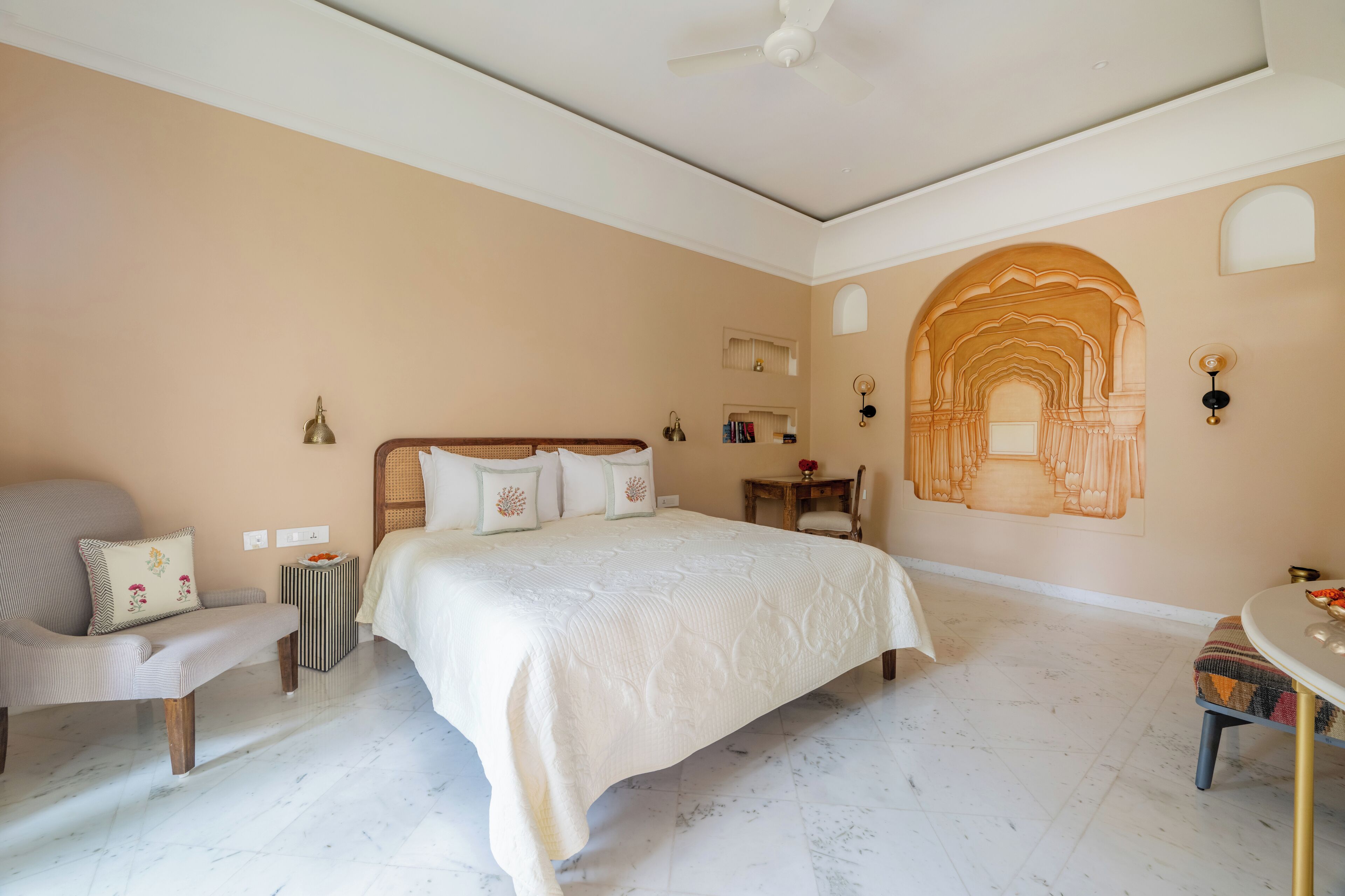 A bedroom with a large bed, a chair, a small table, and a decorative arch on the wall.