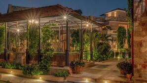 Un espacio exterior bien iluminado con una zona de estar cubierta, senderos de piedra y plantas en macetas.