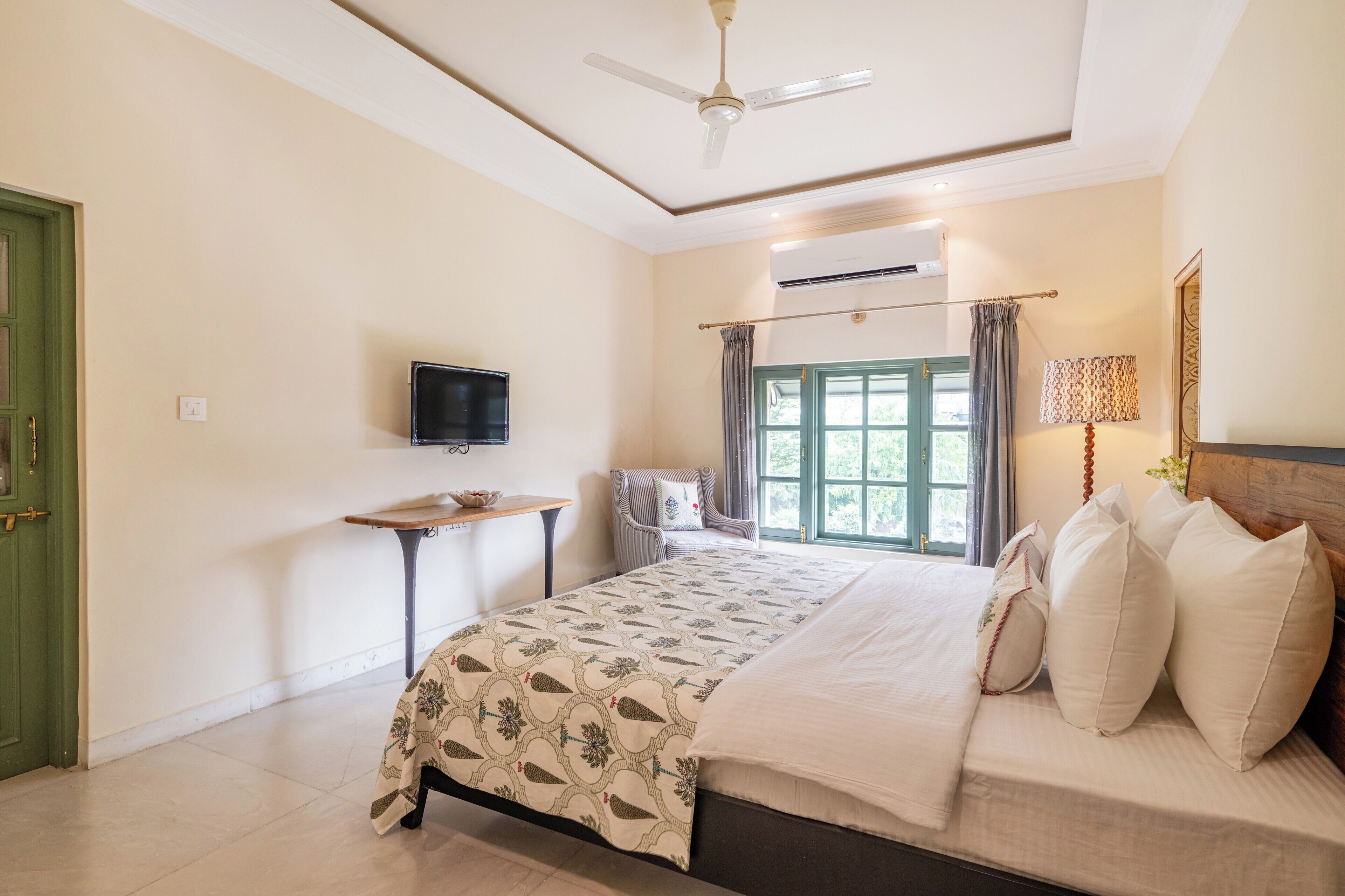 A bedroom with a bed, a television, a window with curtains, a ceiling fan, and an air conditioning unit.