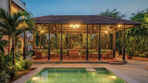 A covered outdoor seating area with a pool, surrounded by lush greenery and a decorative fence. - Niravi Jaipur (Jaipur)