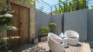 Une terrasse avec des chaises en osier, une porte en bois et des plantes en pot.