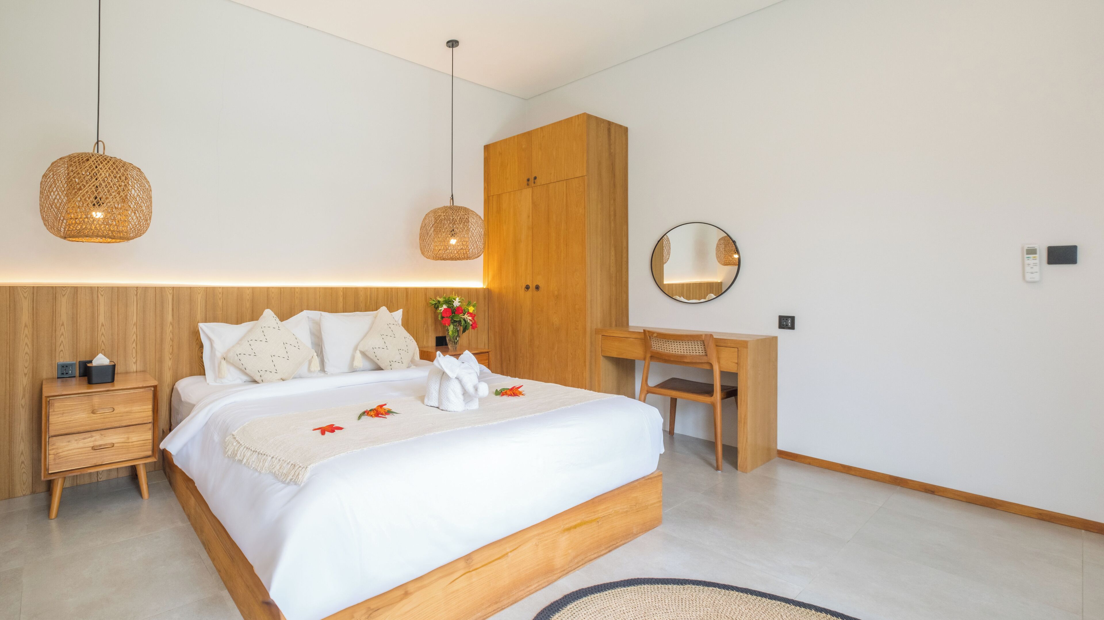 Une chambre à coucher moderne avec une tête de lit en bois, un bureau en bois, un miroir rond et une table de chevet avec une lampe.