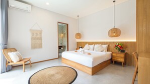 Une chambre moderne avec un grand lit, une tête de lit en bois, des tables de chevet, un fauteuil en osier, une décoration murale en macramé et un luminaire suspendu.
