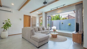 Un salon moderne avec un canapé d’angle, une petite table ronde ornée d’un vase et un téléviseur posé sur un meuble en bois.