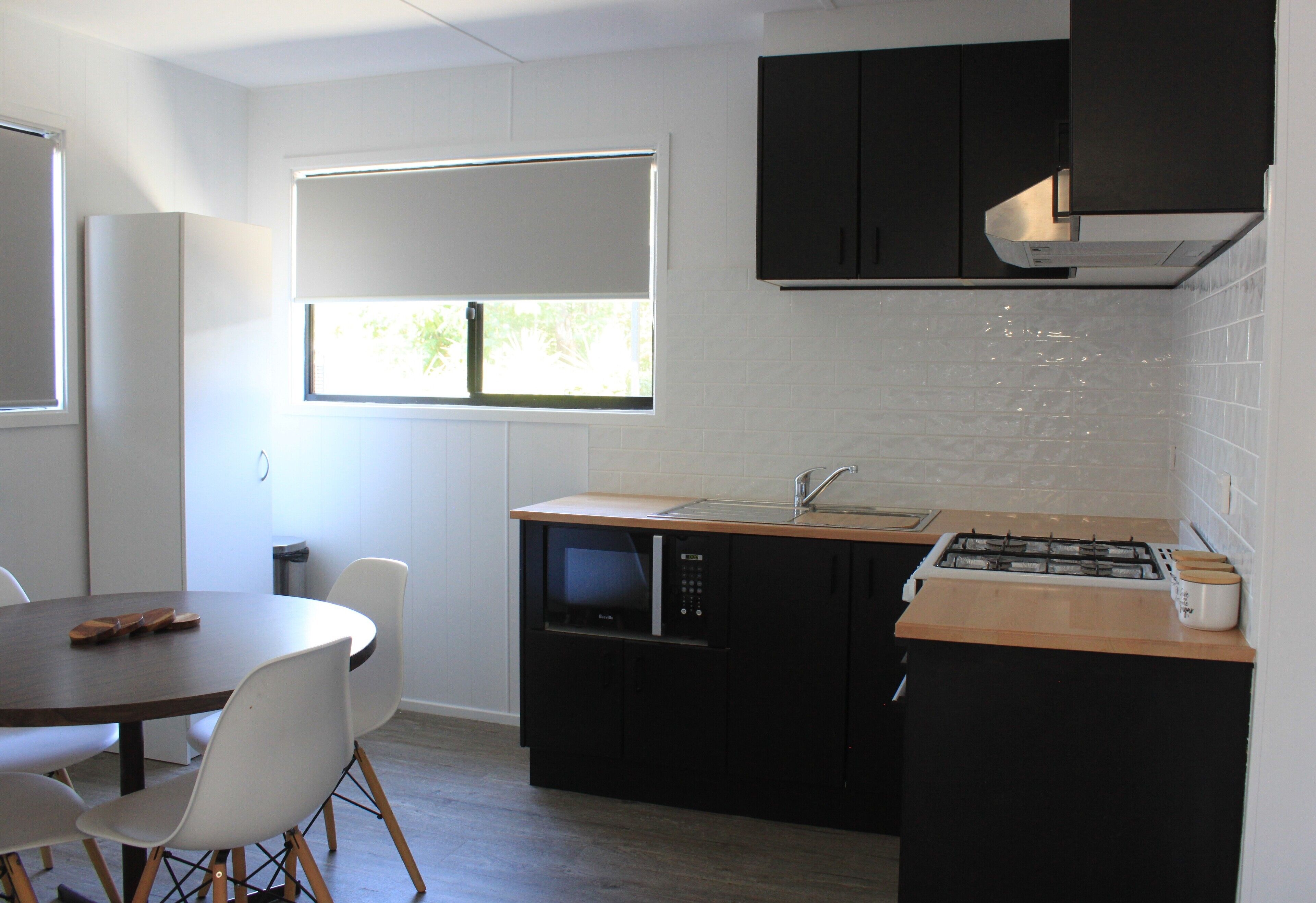 Cozinha compacta com micro-ondas, fogão e armários pretos. Uma janela proporciona luz natural e há uma área de refeições com mesa e cadeiras.