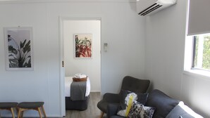 Ein modernes Wohnzimmer mit einem grauen Sofa, zwei Holzstühlen, einem kleinen Tisch und einer Tür zu einem anderen Raum.
