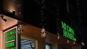 Un bâtiment avec une enseigne indiquant « MI CASA HOMES » et « CHAMBRES DISPONIBLES ». On peut voir des plantes en pot à l’extérieur et une entrée bien visible.