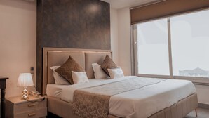Une chambre d’hôtel moderne avec un grand lit, une table de chevet avec une lampe et une vue sur la ville grâce à une grande fenêtre.