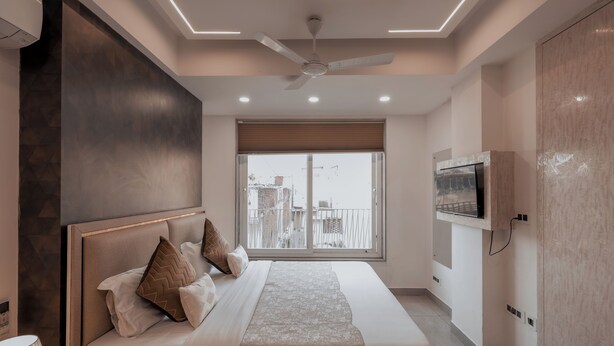 Une chambre à coucher moderne avec un grand lit, un ventilateur de plafond et un téléviseur fixé au mur.