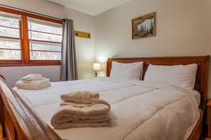 Una cama bien tendida con sábanas blancas y una pila de toallas dobladas.