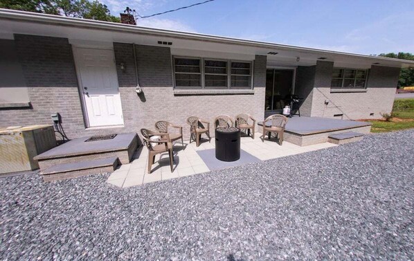 Relax on the patio with wicker chairs and a small table, surrounded by a brick exterior and gravel ground.