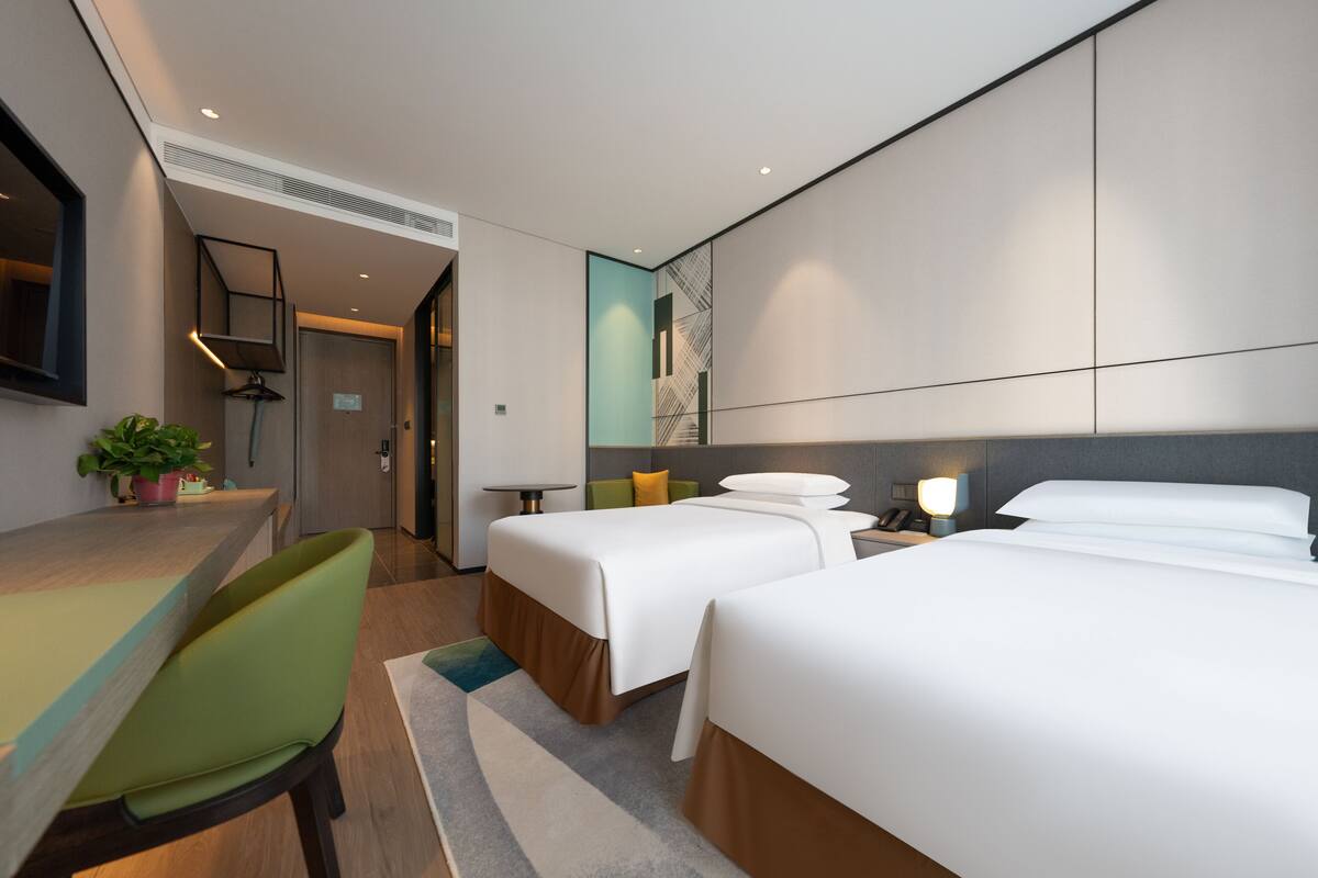 A modern hotel room with two beds, a desk, and a chair.