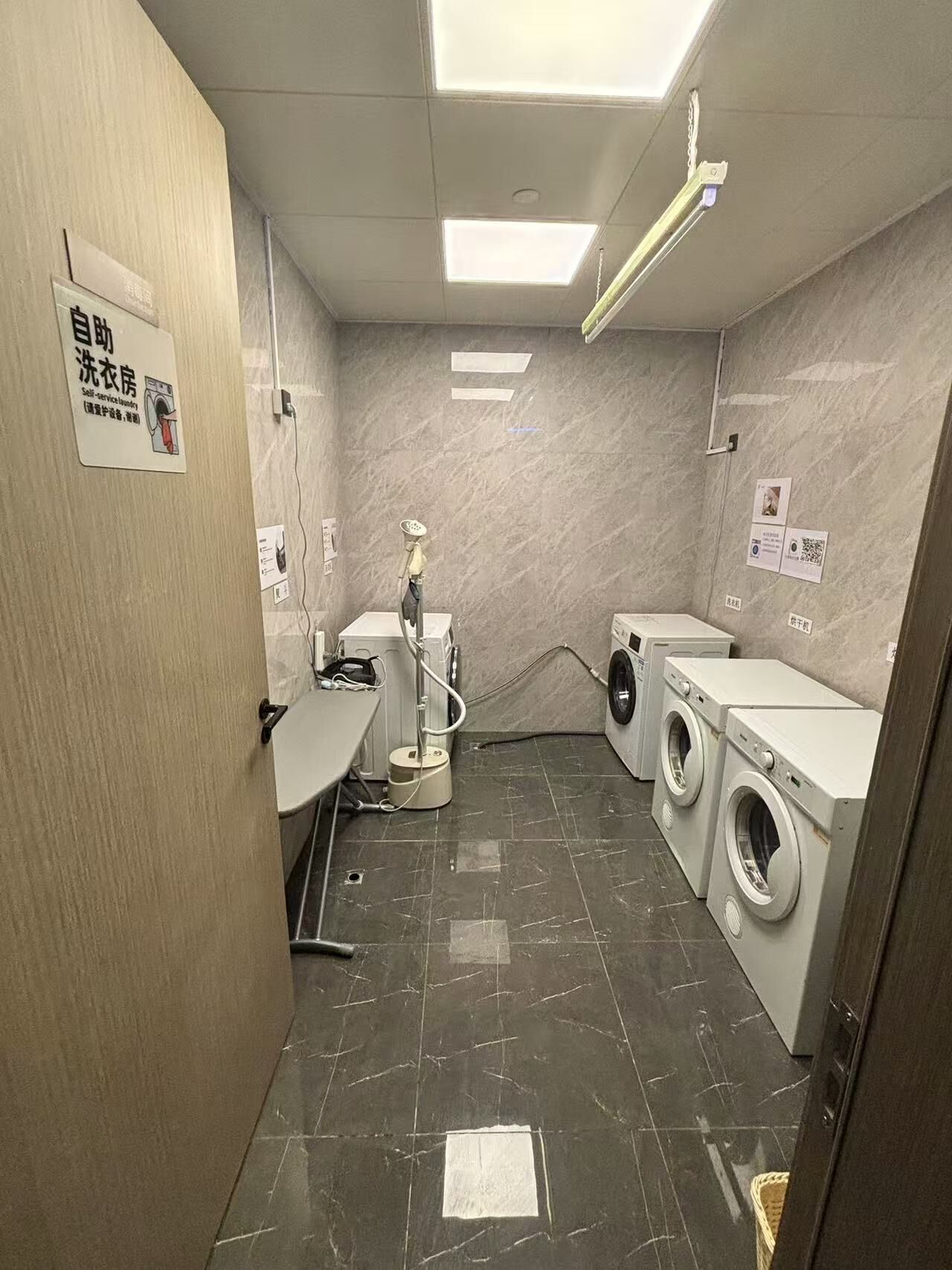 A self-service laundry room with a washing machine, dryer, and a hose for washing.