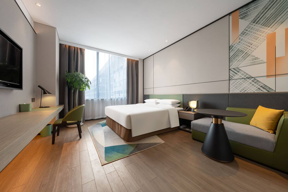 A modern hotel room with a bed, a sofa, a desk, and a TV.