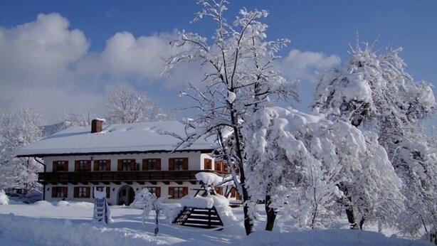 Ein schneebedecktes Gebäude im traditionellen Stil, umgeben von Bäumen und einem klaren Himmel.