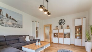 Un salon moderne avec un canapé gris, une table basse en bois, un tapis rond, une horloge murale et des étagères intégrées.