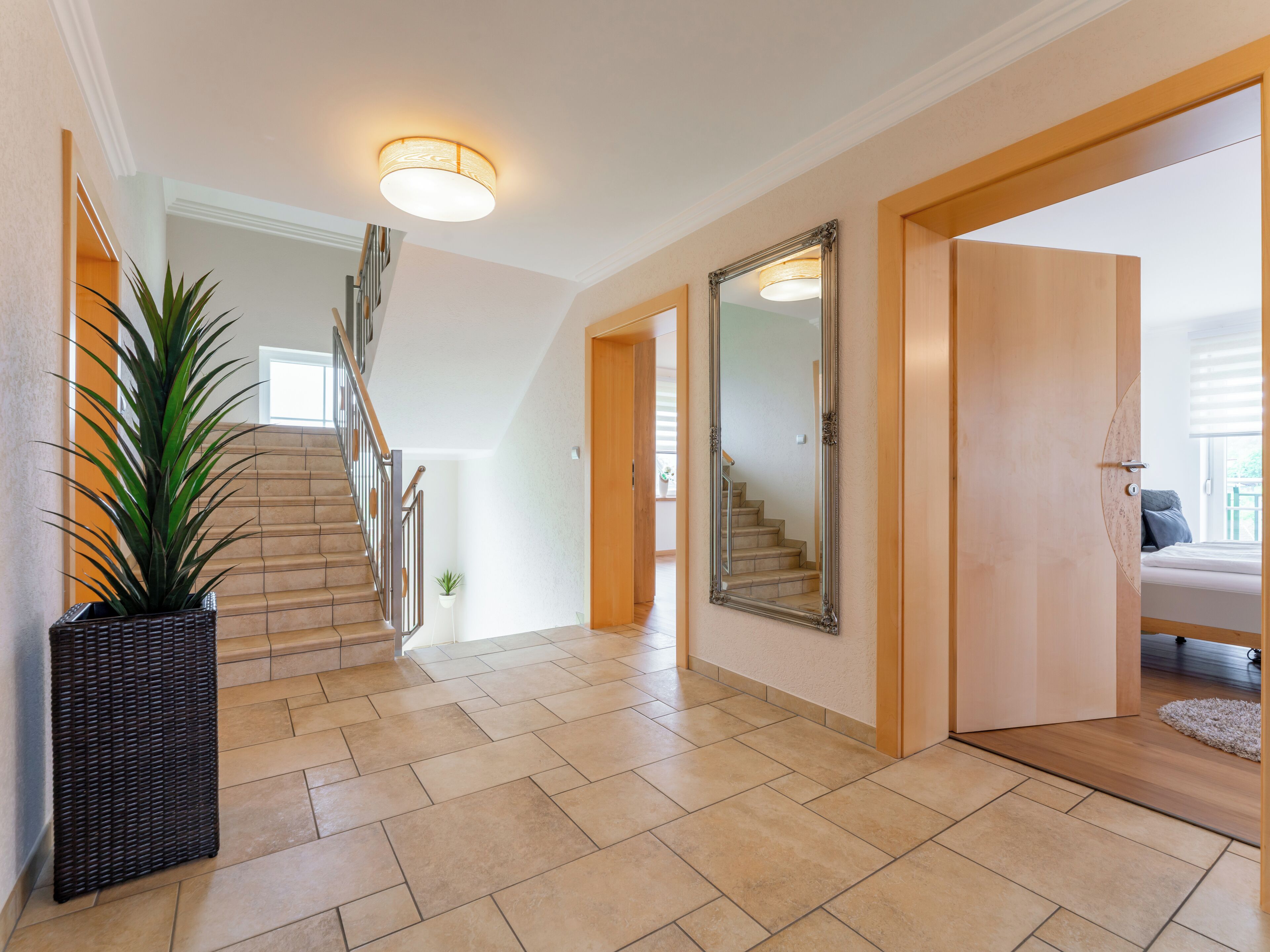 Ein geräumiger Flur mit Treppe, einem großen Spiegel und einer Zimmerpflanze.