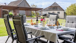 Un espace de restauration en plein air avec une table dressée pour quatre personnes, entourée de chaises, et une pergola en arrière-plan.