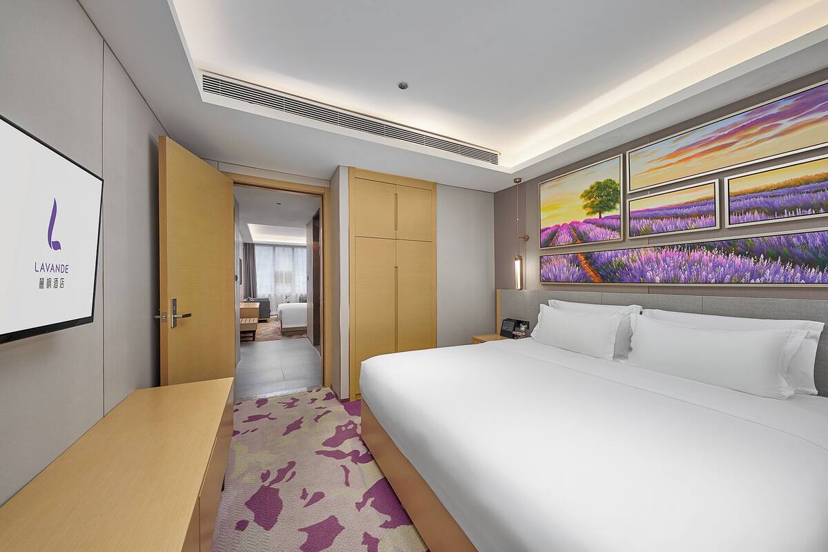 A hotel room with a large bed, a desk, and a painting of lavender fields on the wall.