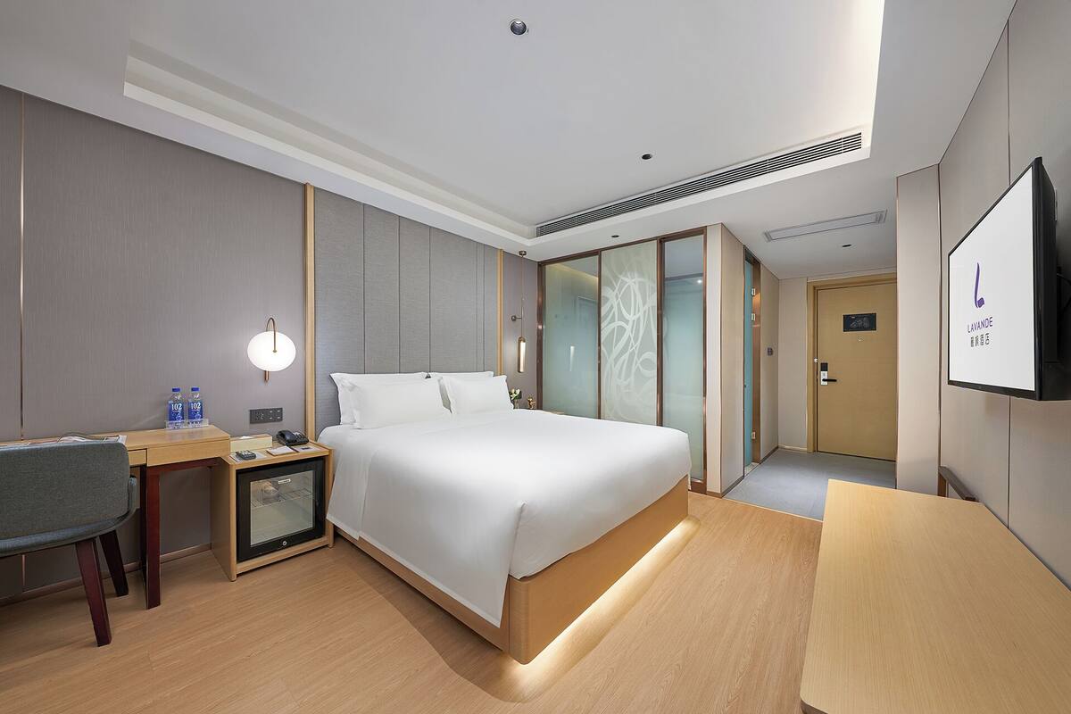 A hotel room with a large bed, bedside tables, a desk, a chair, and a TV.