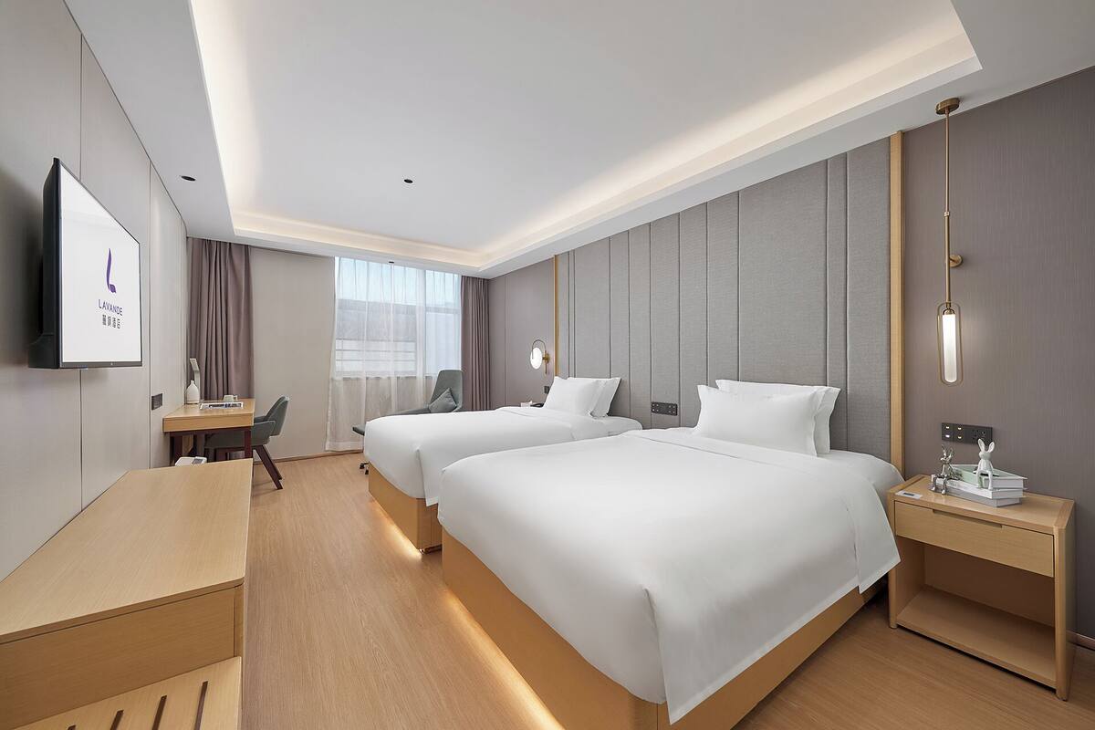 A hotel room with two beds, a desk, a chair, a TV, and a window with curtains.