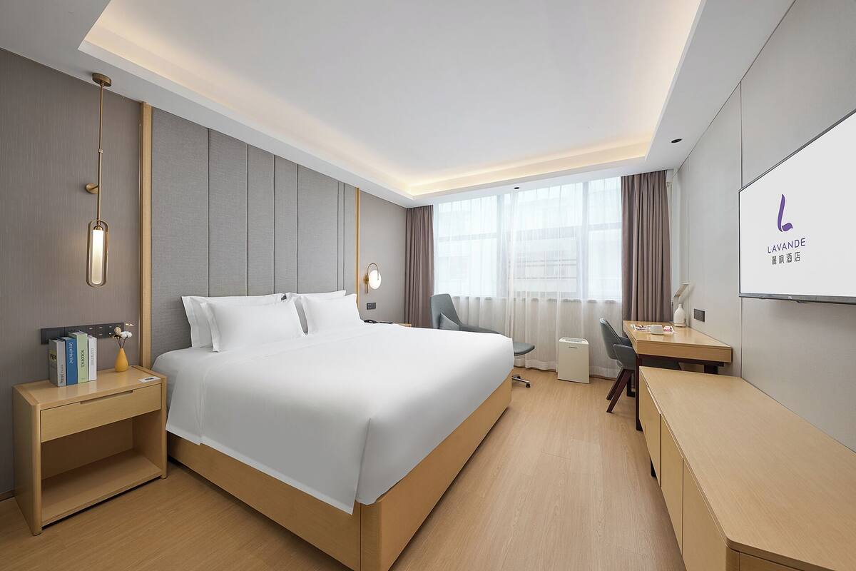 A hotel room with a large bed, bedside tables, a desk, and a TV.