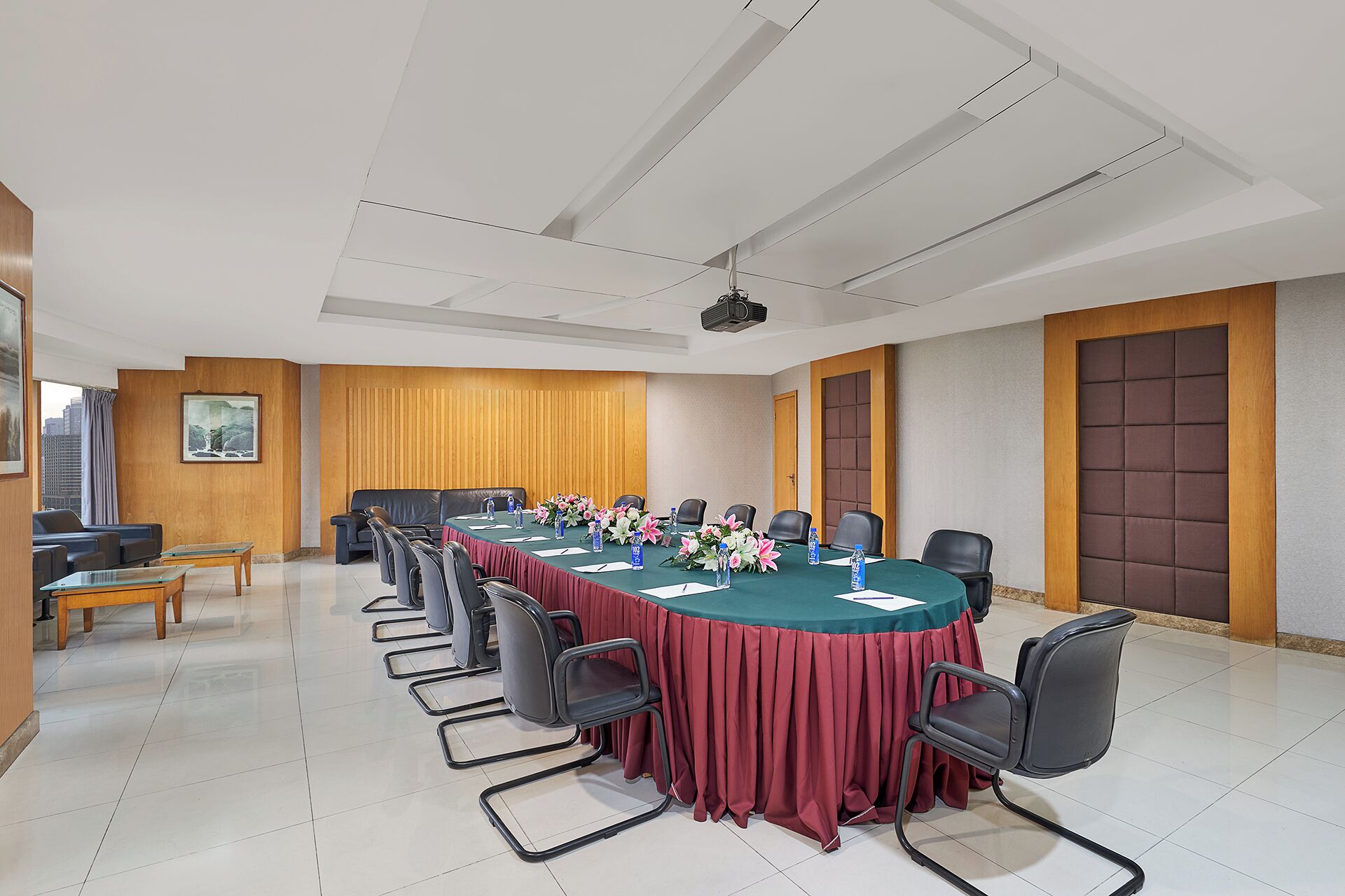 Un salón de conferencias con una larga mesa, sillas, un proyector y un amplio ventanal con vistas a la ciudad.