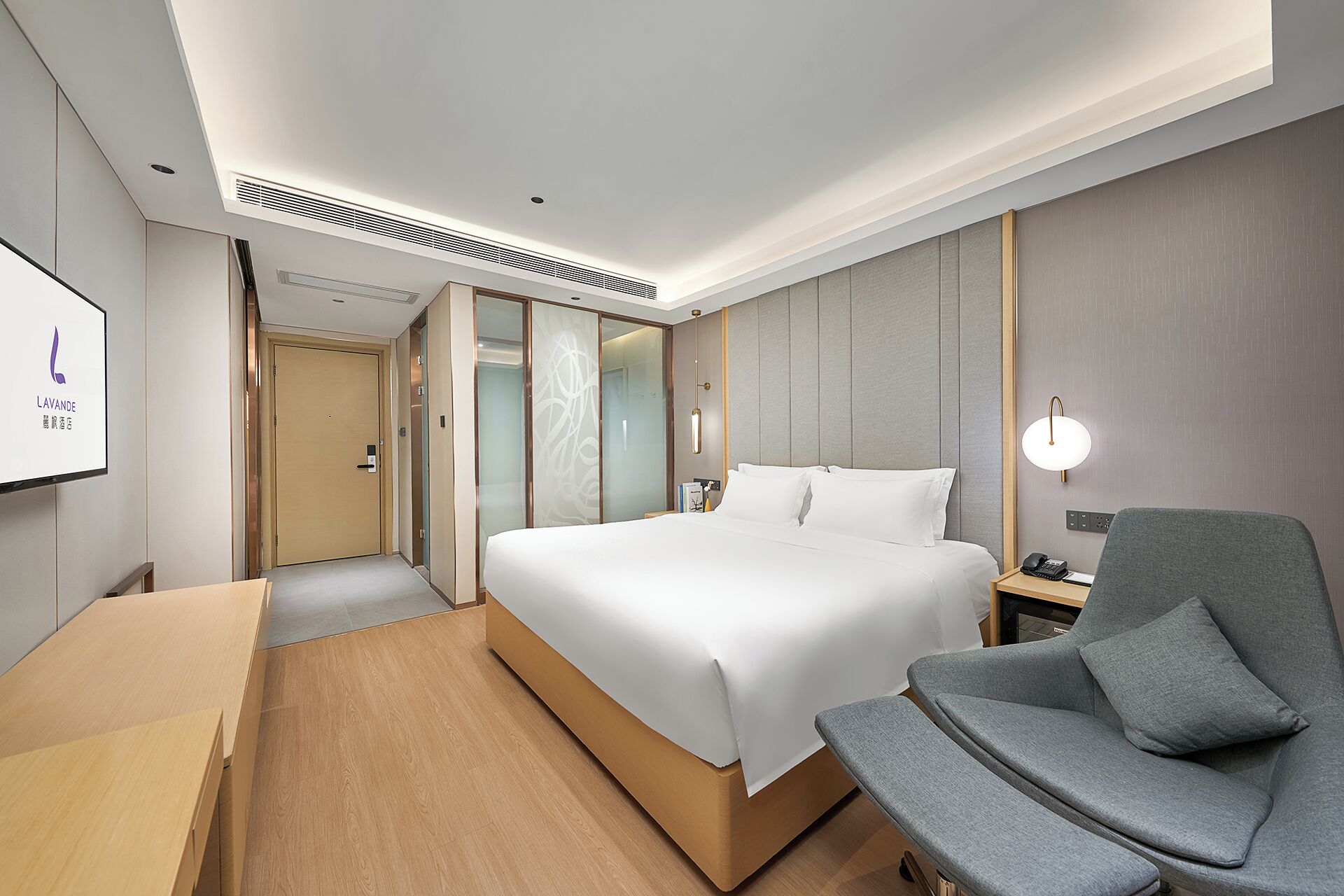 Een hotelkamer met een groot bed, een bureau, een stoel en een aan de muur bevestigde televisie.