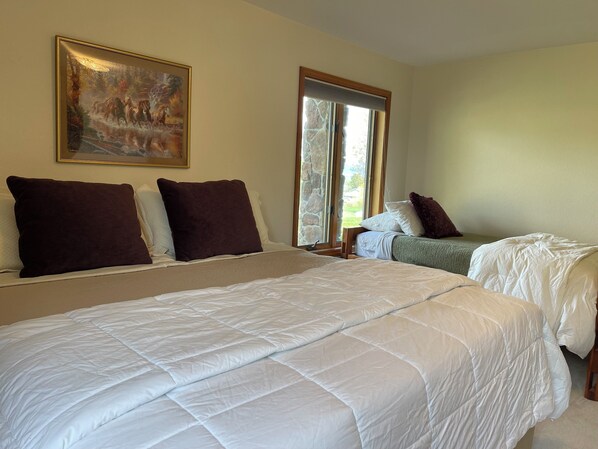 A hotel room with a large bed, a painting on the wall, and a window with a view of the outdoors.