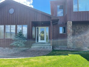 A modern two-story house with a stone accent wall, a front porch, and a small evergreen tree.