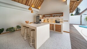 Una cuina moderna amb una illa central, tamboretes de bar, armaris de fusta i un sostre amb bigues al descobert.
