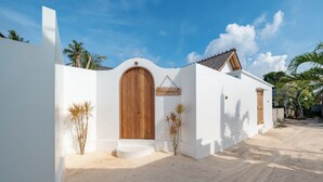 Una vila blanca amb una porta de fusta i un rètol que diu "Villa Lacona" en una zona sorrenca amb palmeres.