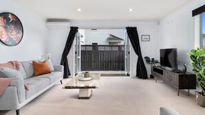 Una sala de estar moderna con un sofá gris, una mesa de centro, un televisor en un mueble y vistas al exterior a través de un ventanal.