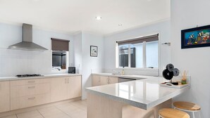 Una cocina moderna con una isla central, taburetes de madera, una campana extractora de acero inoxidable y una ventana con vistas.
